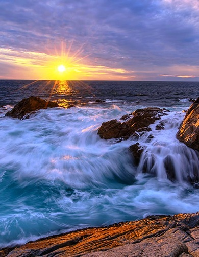 Gorgeous, satin blue Pacific Ocean sunset with waves washing on the rocky shore.